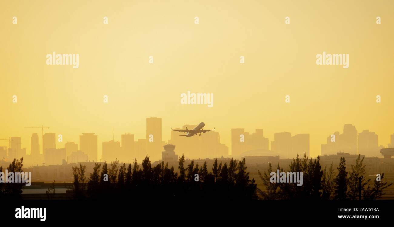 Beim Start vom Flughafen Miami mit der Stadt im Hintergrund wird ein Flugzeug vor einem farbenfrohen Sonnenaufgang in Gelb und Orange silhouettiert. Stockfoto