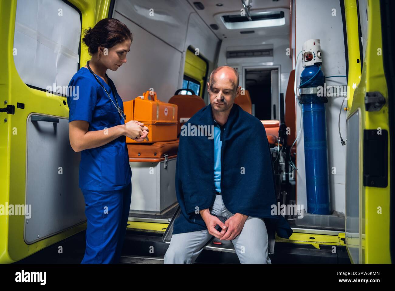Die Krankenschwester in medizinischer Uniform betrachtet den Mann, der auf dem Krankenwagen in der Decke sitzt Stockfoto