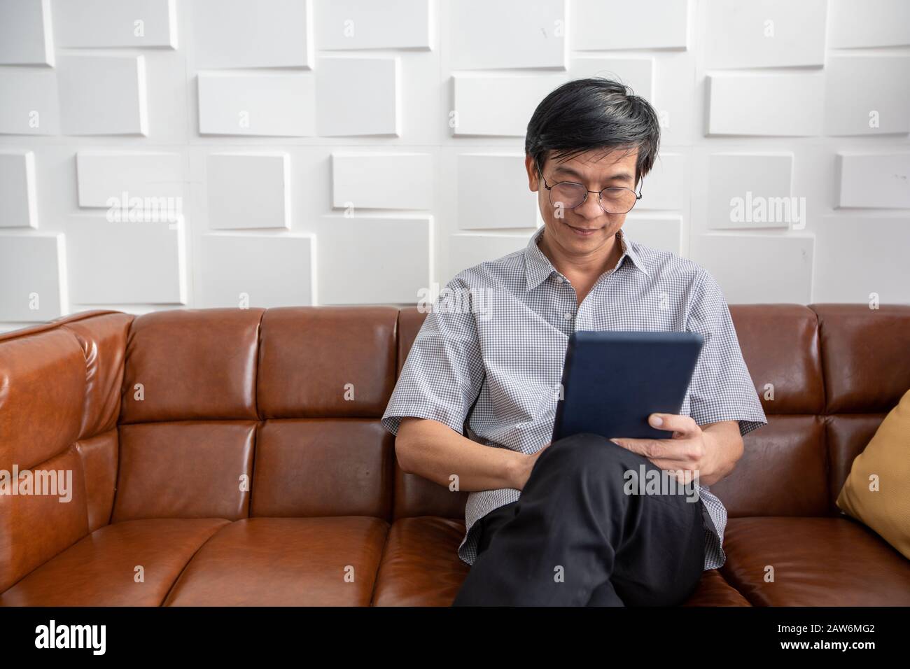 Senior Asian man spielt Tablet auf dem Sofa im Wohnzimmer zu Hause Portrait des asiatischen älteren Mannes ist Entspannend und Glücklich Mit spielendem Tablet Stockfoto