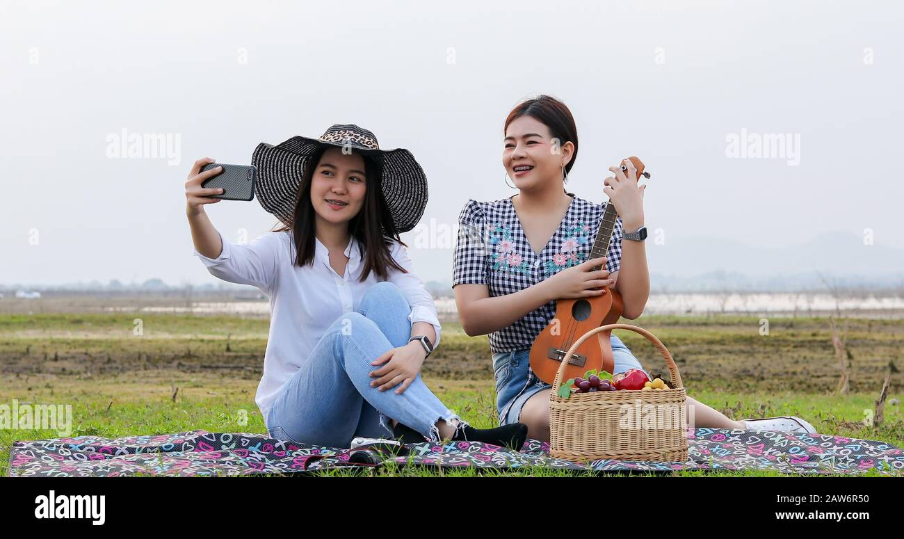 Eine Gruppe asiatischer Freunde, die Ukelele spielen und in den Sommerferien Zeit für ein Picknick verbringen.Sie sind glücklich und selfie, Entspannungszeit auf der Ferienkcon Stockfoto