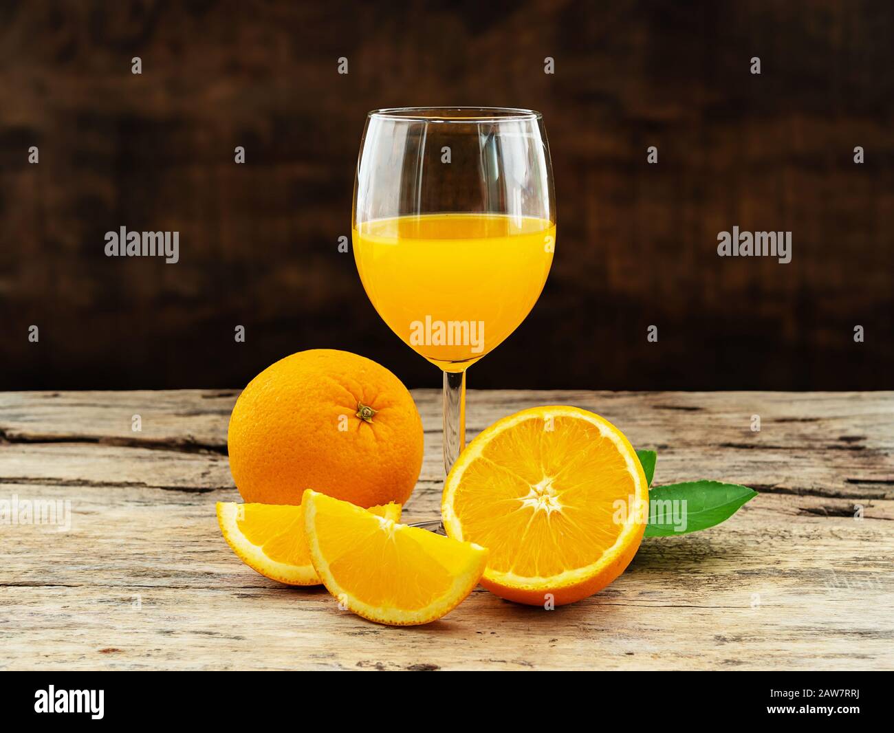 Ein Glas frischen Orangensaft und eine Gruppe frischer Orangenfrüchte mit grünen Blättern auf Holzhintergrund. Obstprodukt-Display oder Montage, Studioaufnahme Stockfoto