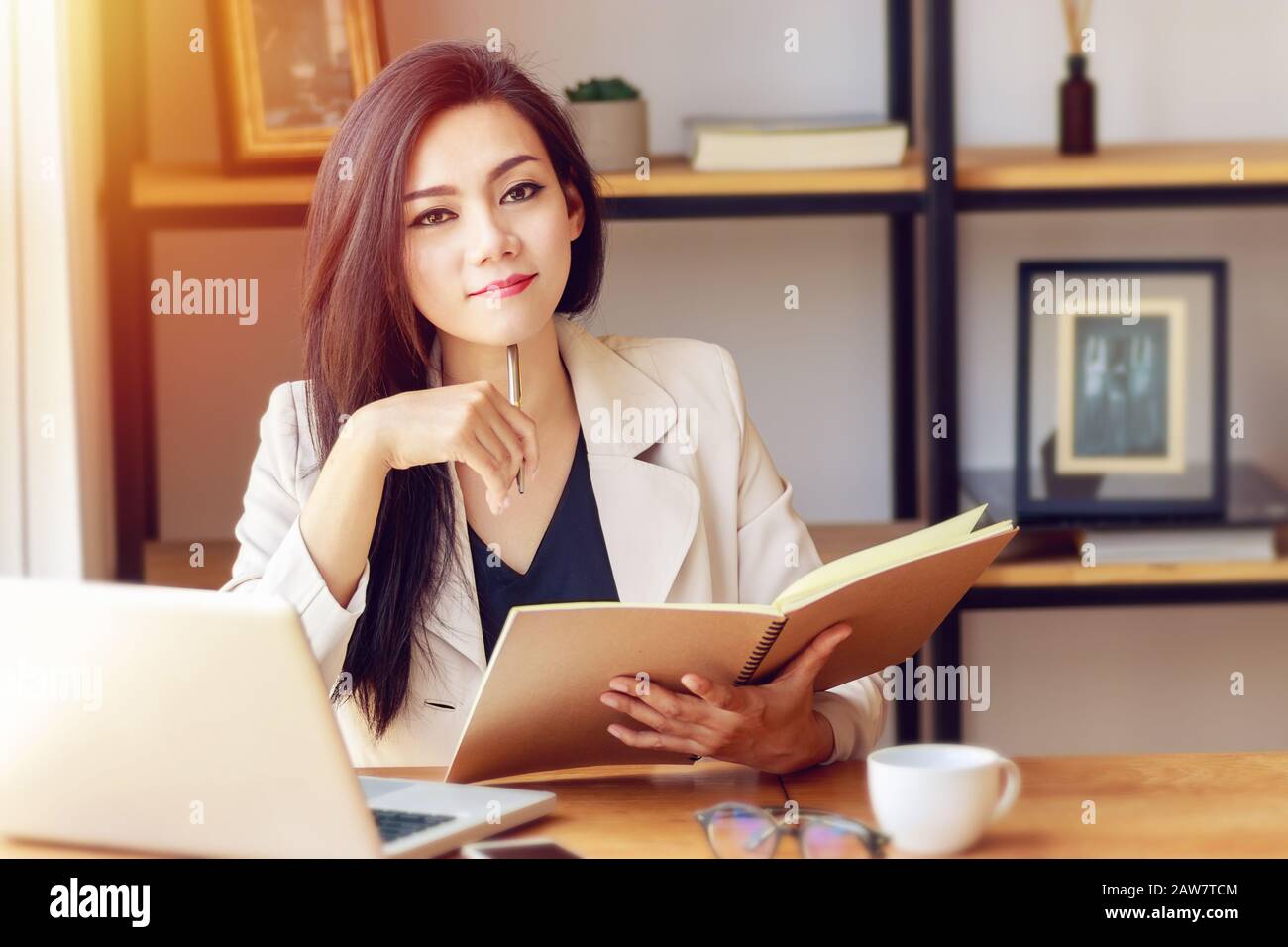 Porträt der schönen und selbstbewussten asiatischen Geschäftsfrau in der Arbeit mit Notebook Laptop und Buch verwalten Arbeit am Arbeitsplatz, Blick auf Kamera und smi Stockfoto