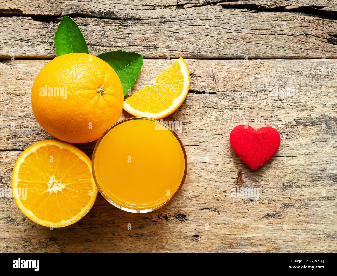Ein Glas frischen Orangensaft und eine Gruppe frischer Orangenfrüchte mit grünen Blättern, auf Holzhintergrund mit roter Herzform, Vitamin C und Fruchsprodu Stockfoto