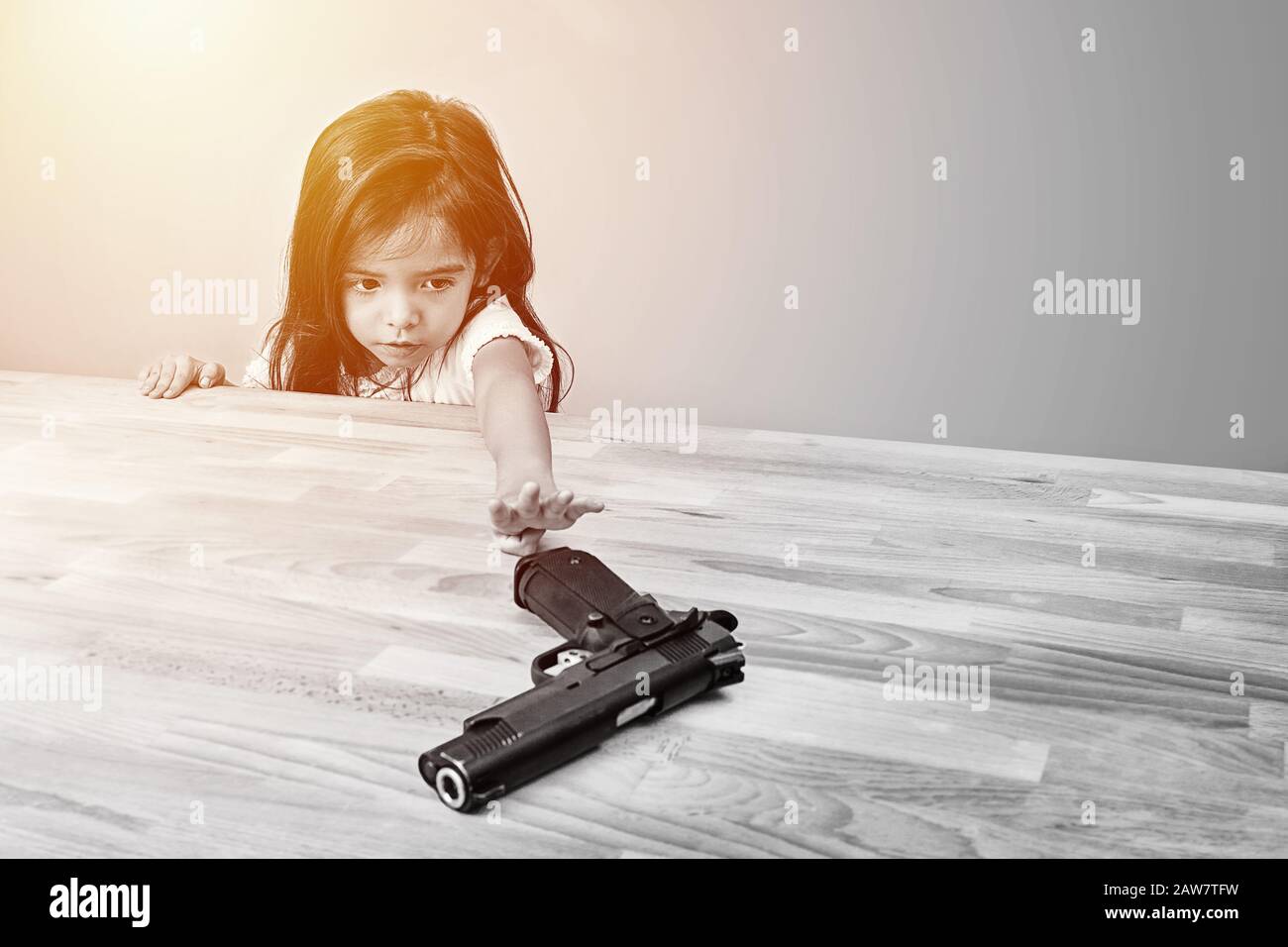 Sicherheit und Unfall im Heimkonzept. Kinder versuchen, die Waffe der Eltern auf dem Tisch zu spielen. Monotone Farbe Stockfoto