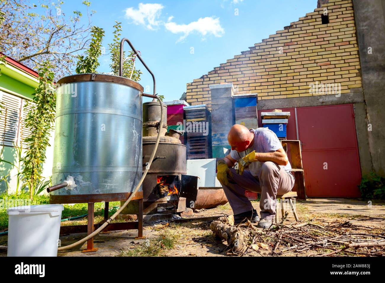 Der Mann wirft trockene Äste in die Feuerbox einer hausgemachten Destillerie, die Mondschein-Schnaps, alkoholische Getränke, zubereitet. Stockfoto