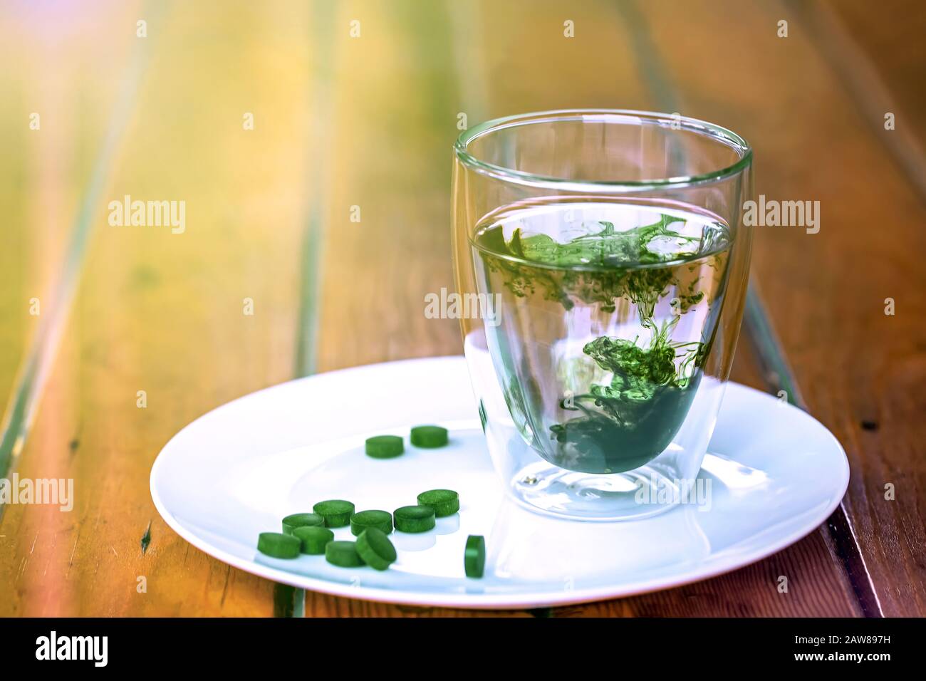 Chlorophyll in einem Glas Wasser und grüne Pillen Spirulina auf einem Teller auf Holztisch. Kopierraum, Sonnenlicht. Stockfoto