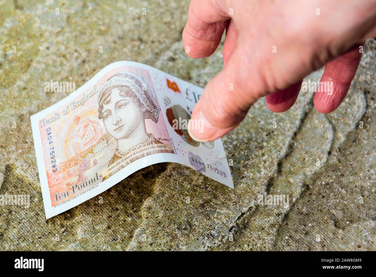 Ein glücklicher Rentner findet Geld auf dem Boden Hand reicht bis zu holen eine neue zehn Pfund Note Pfund vom Boden. England Großbritannien Stockfoto
