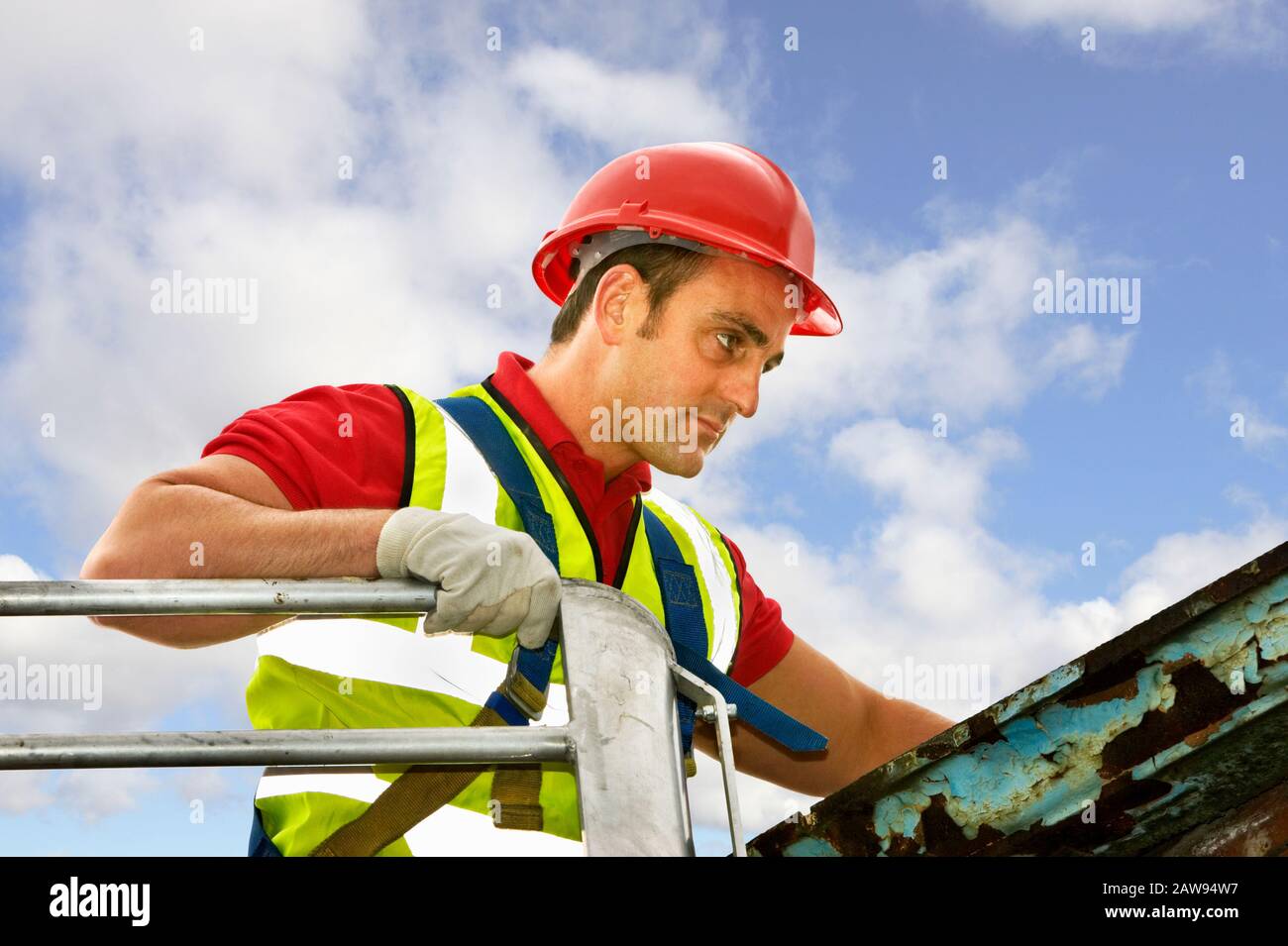Arbeitsmann in einem Kirschpflücker, der Sicherheitskleidung trägt und ein Dach inspiziert Stockfoto