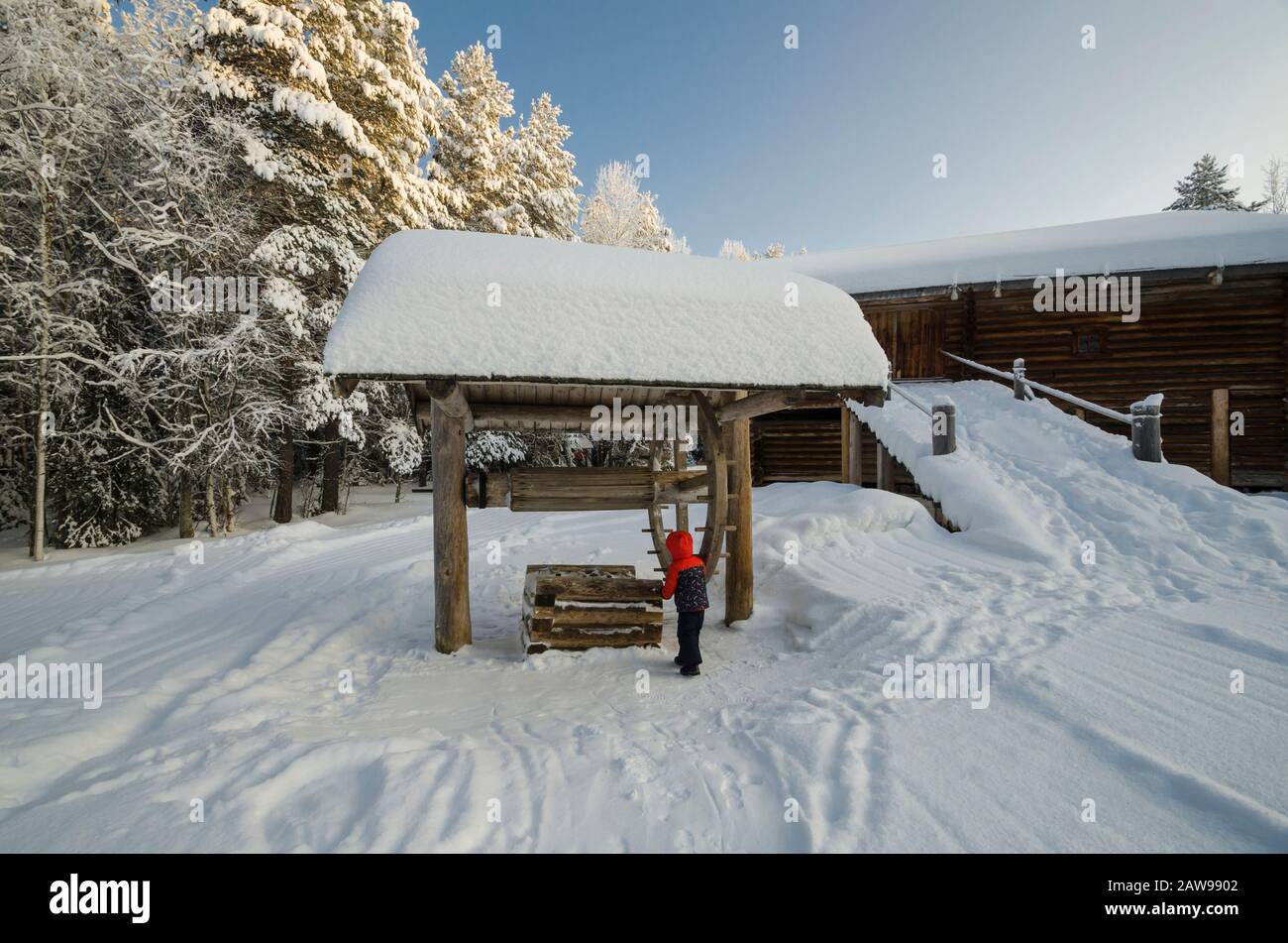 Januar 2020 - Malye Korely. Kleiner Junge an einem Holzbrunnen in einem russischen Dorf. Russland, Region Archangelsk Stockfoto