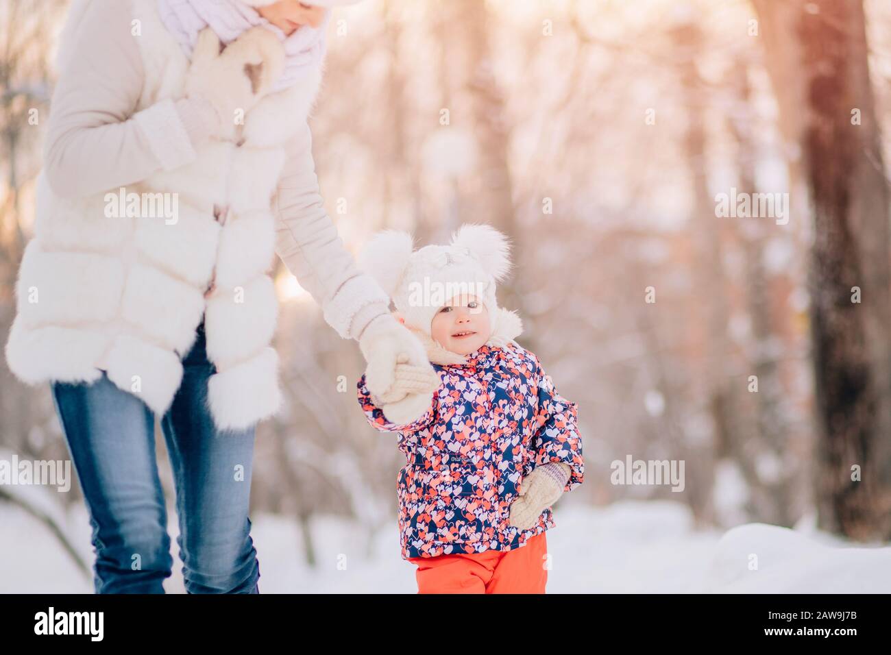 Im Winter spaziert die Krankenschwester mit dem Kind draußen und hält seine Hand fest mit den Fellen und der Fellweste im Morgengrauen Stockfoto