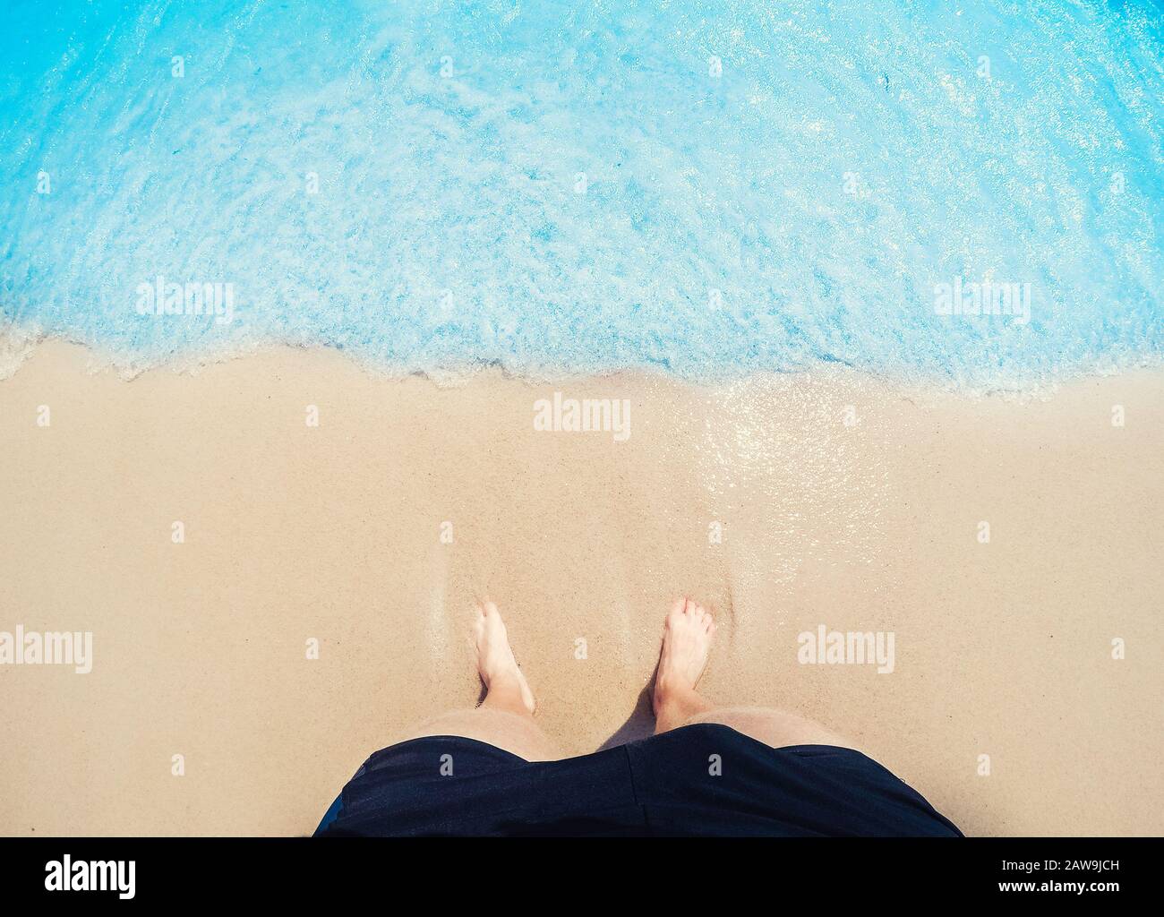 Füße des Menschen Fuß in goldenem Sand werden von Wellen des blauen Meeres gewaschen, Draufsicht. Freelance-Freelancer-Konzept. Stockfoto