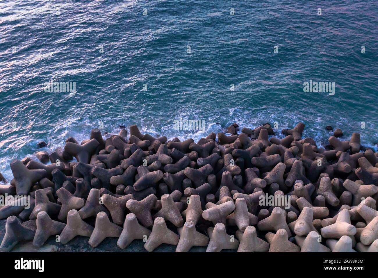 Künstliches Riff von Felsen am Ufer vor dem Meer. Die Zusammensetzung von ineinander greifenden Steinen bildet das Design als Textur. Stockfoto