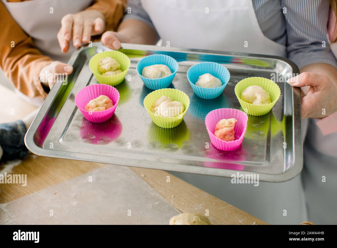 Vorbereiten von Muffins zum Backen. Teig in silikonfarbige Tassen aufgeteilt, die auf einem Backblech aus Metall Liegen. Nahaufnahme der Hände von Frauen, die Muffin-Backtra halten Stockfoto