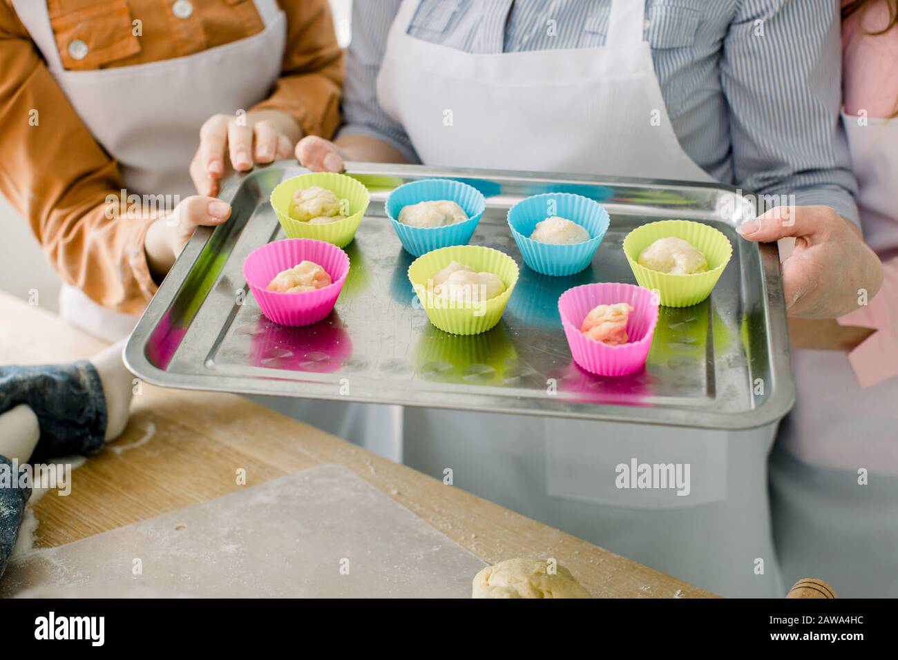 Vorbereiten von Muffins zum Backen. Teig in silikonfarbige Tassen aufgeteilt, die auf einem Backblech aus Metall Liegen. Nahaufnahme der Hände von Frauen, die Muffin-Backtra halten Stockfoto