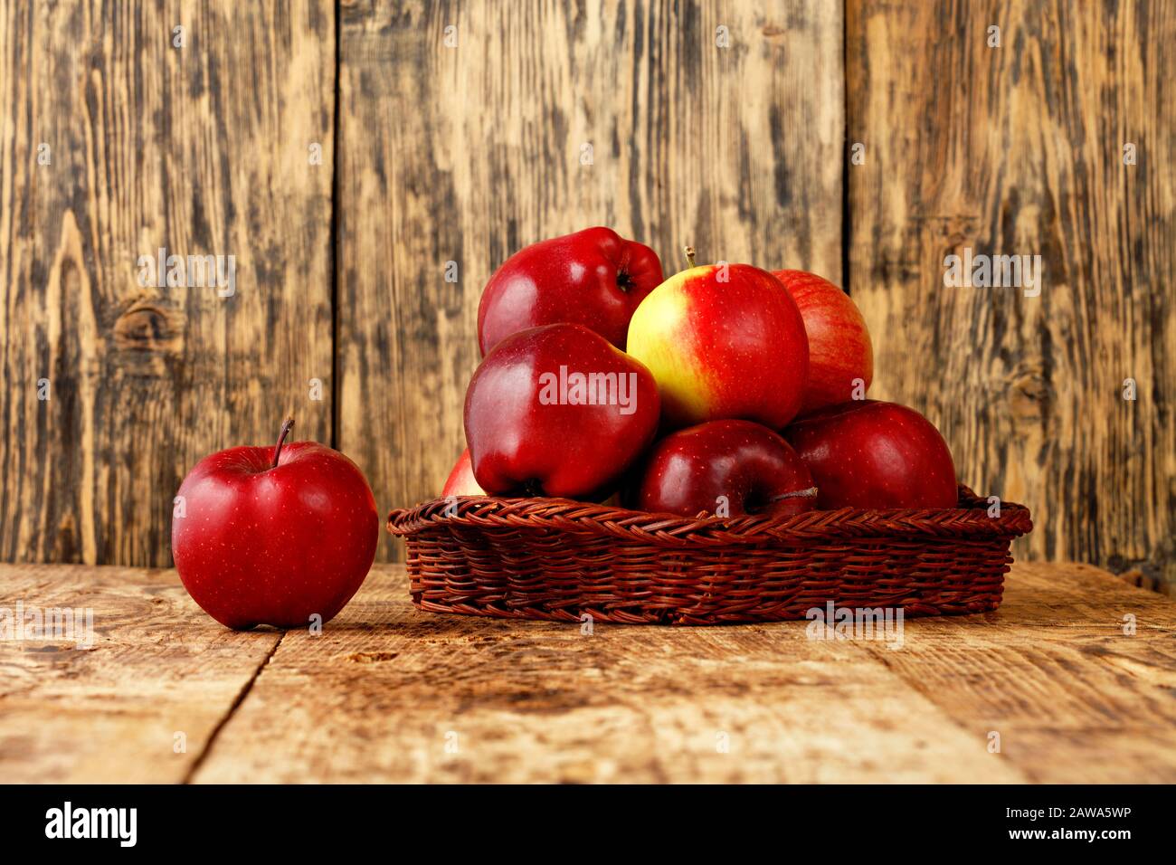 Rote reife Äpfel liegen in einem Korbkorb auf einem alten Holztisch auf Holzhintergrund, Bild mit Kopierraum. Stockfoto