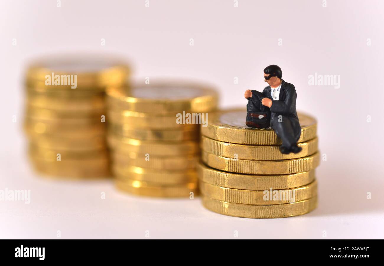 Modell des Mannes, der eine Sonnenbrille trägt und in der Jackentasche schaut, während er auf einem Stapel von Münzen mit einem Pfund sitzt. Stockfoto