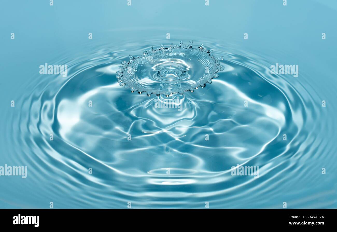 Tropfen von sauberem und frischem Wasser fallen aus einer Höhe von klarem, transparentem blauem Wasser, das Spritzer in Form von Originalfiguren bildet. Stockfoto