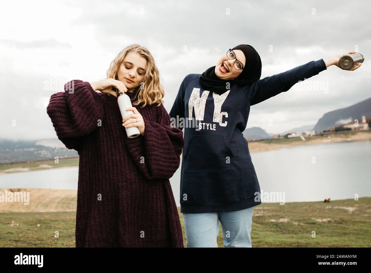 Lifestyle-Porträt zweier bester Freunde, lächelnd und zusammen Kaffee trinken. Foto im Freien von zwei jungen Frauen, eine mit Hijab, die sich gegenseitig genießen Stockfoto