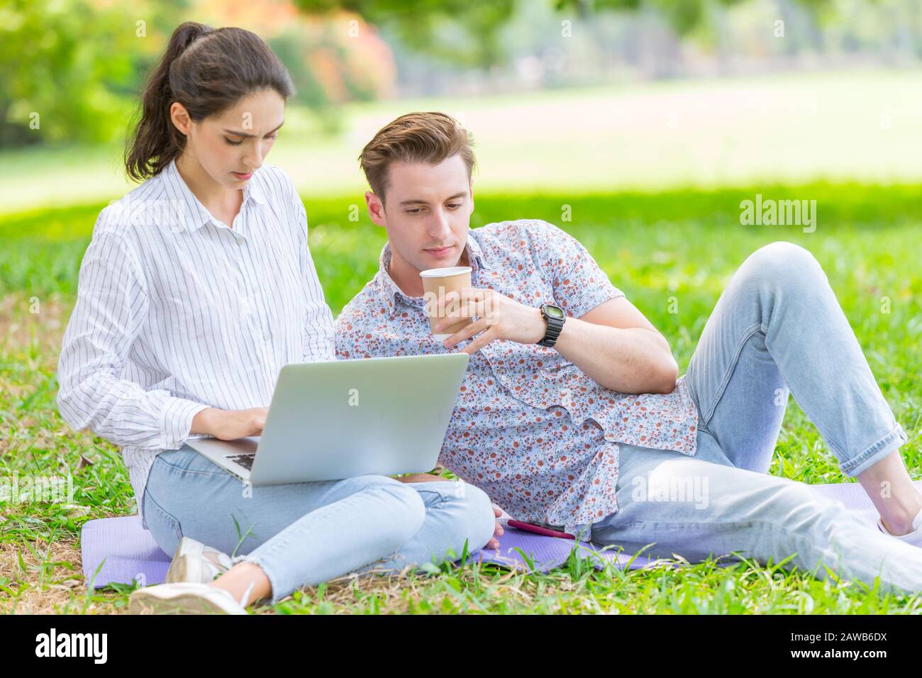 Ein Paar Männer und Frauen, die in Teenagern arbeiten, benutzen einen Laptop, um im Urlaub im Außenpark zu arbeiten Stockfoto