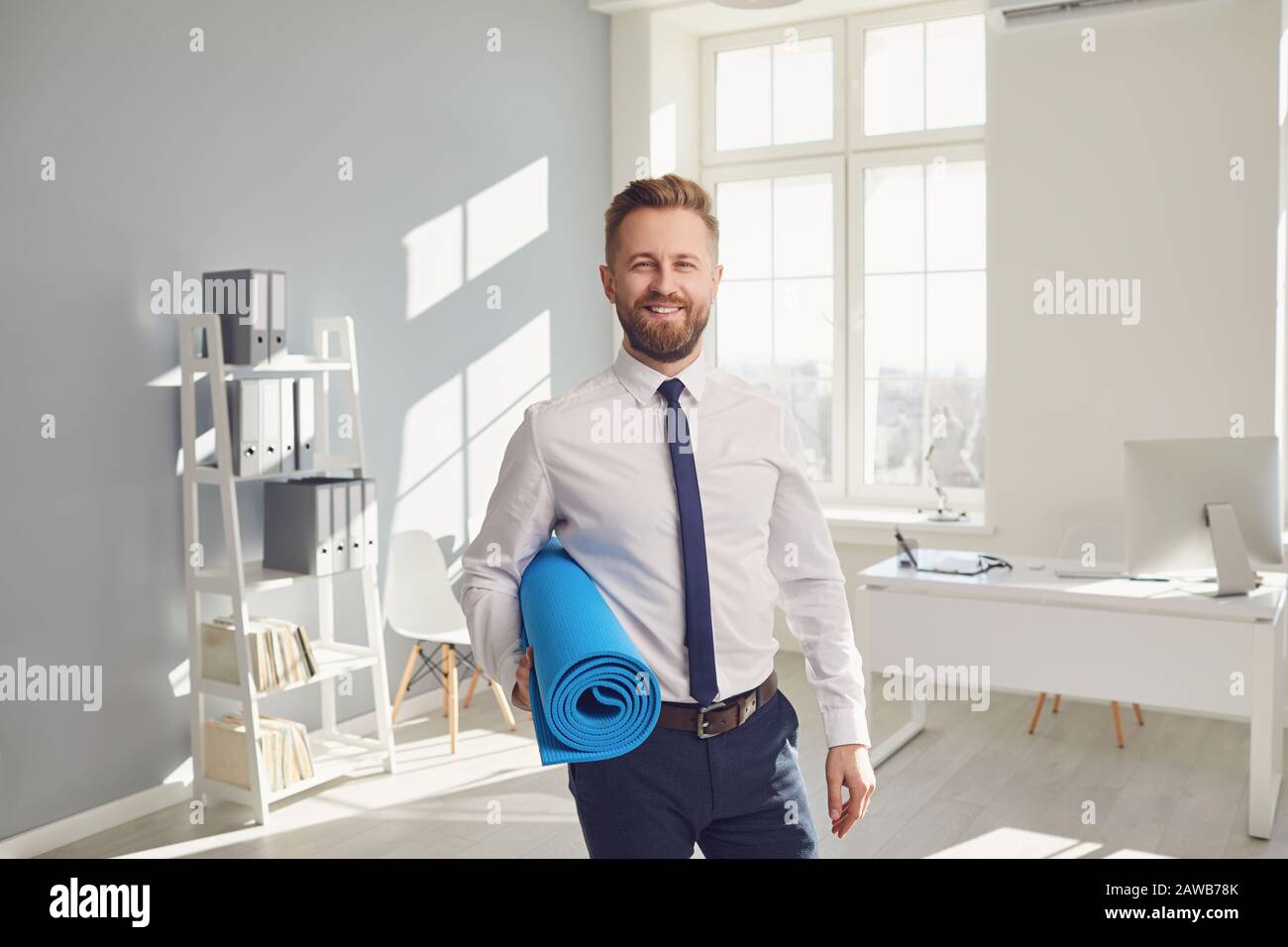 Glücklicher erfolgreicher Geschäftsmann in einem weißen Hemd mit Yogamatte im Büro. Stockfoto