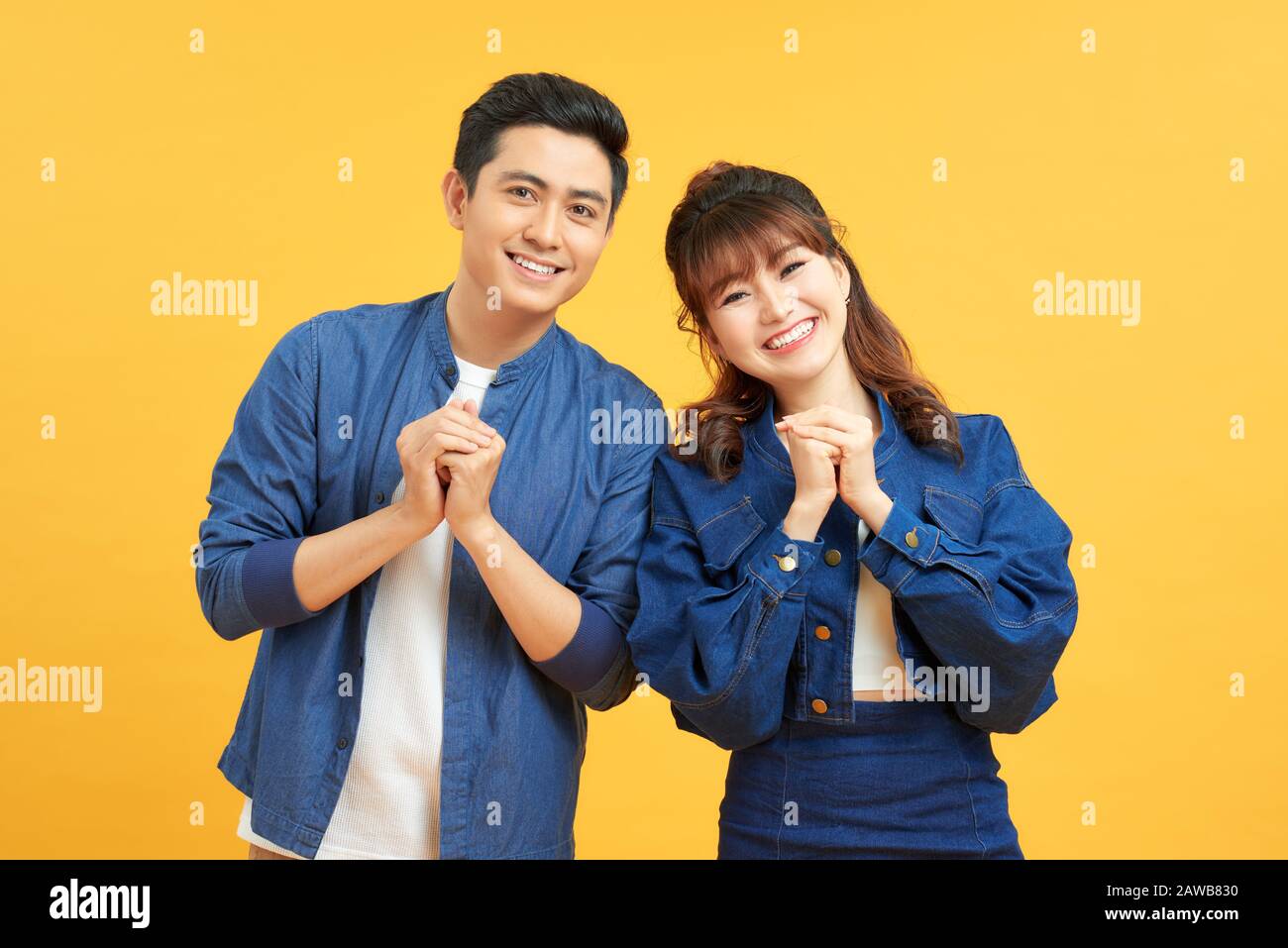Junge Paare posieren in einem gelben Hintergrund, die Hände an der Kamera mit Glückwunsch Geste einklammern. Stockfoto