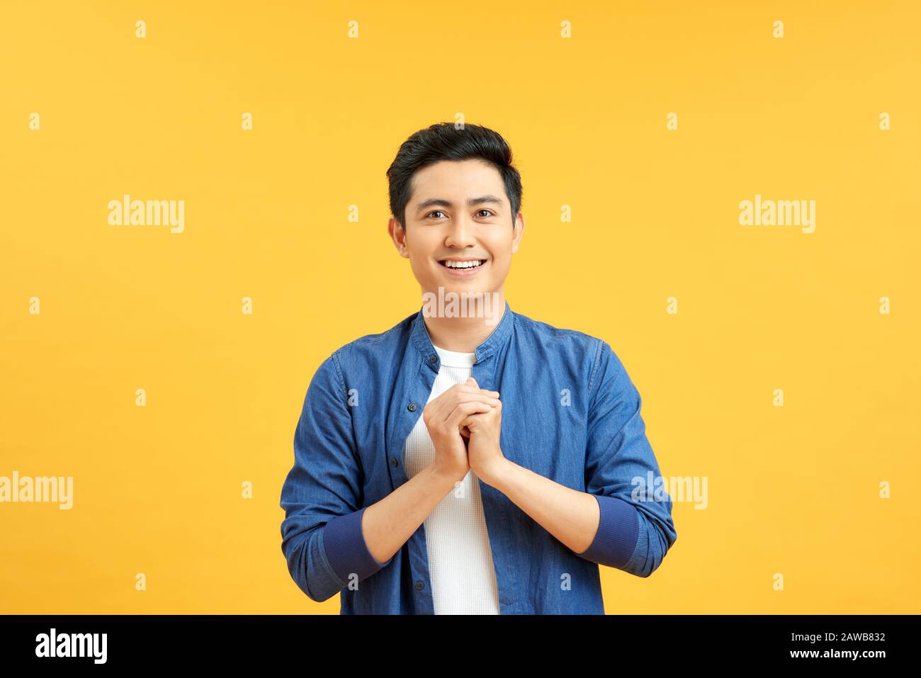 Junger asiat klammert die Hände und blickt auf die Kamera vor gelbem Hintergrund Stockfoto