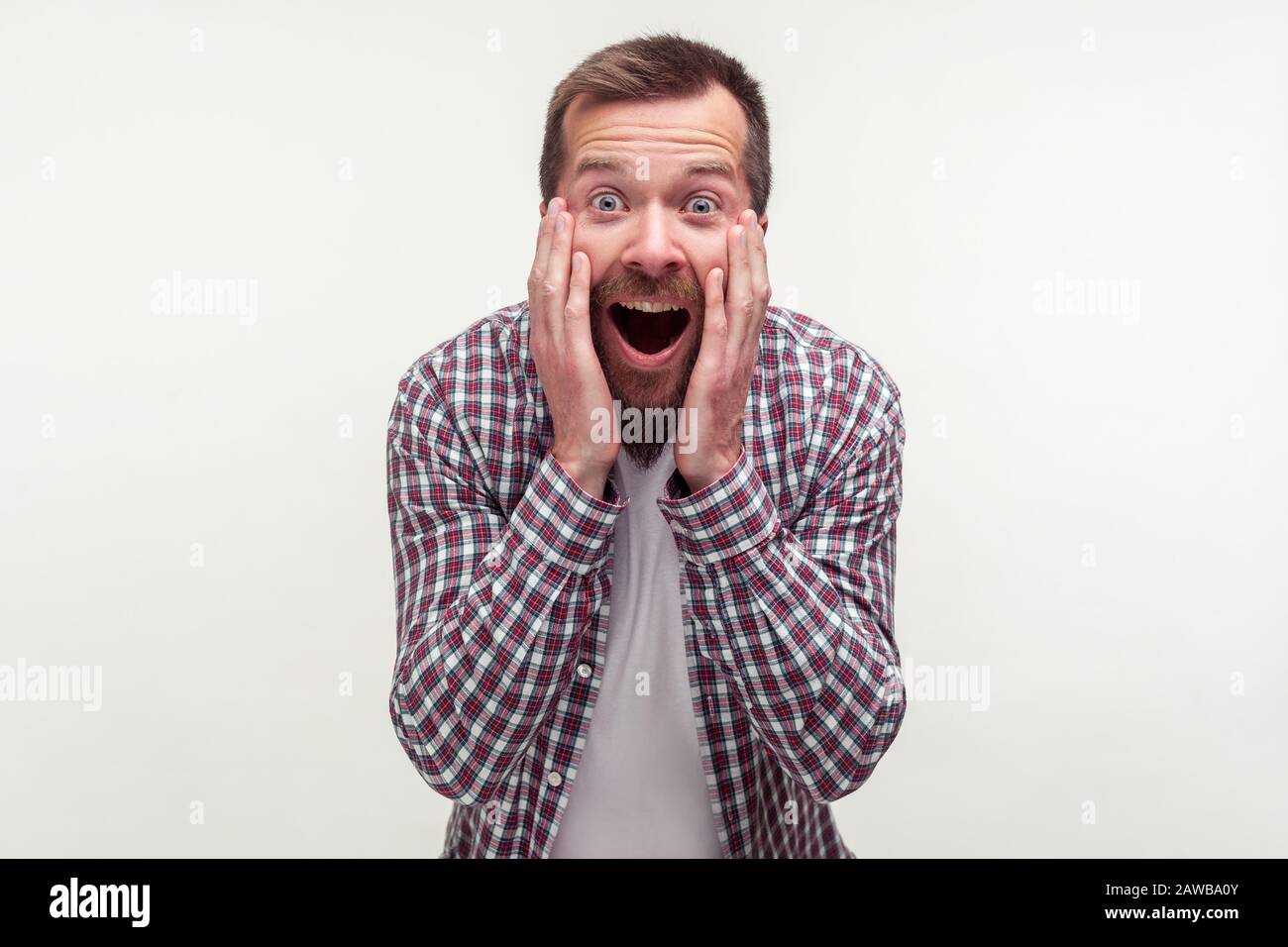 Oh mein gott! Porträt eines schockierten, bärtigen Mannes in einem Plaid Hemd, das die Arme zum Kopf hebt und in Angst schreit und mit großen, verblüfften Augen auf die Kamera starrt. Stockfoto