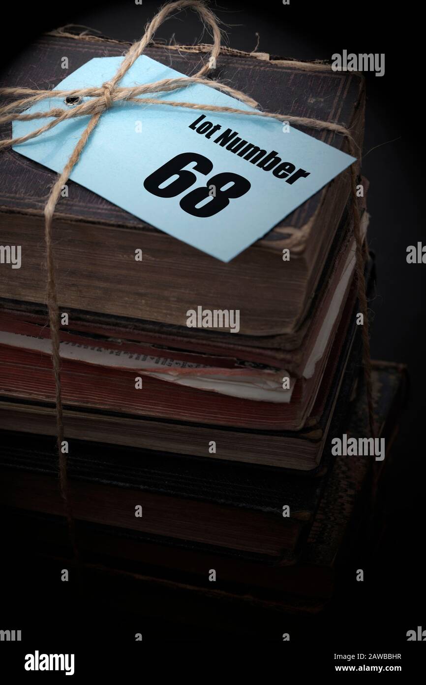 Antike alte Bücher, die in einen Stapel gestapelt sind, der mit einer Schnur mit Auktionshausnummer auf einem blauen Tag-Label verbunden ist. Antiquitäten Auktionskonzept Stockfoto