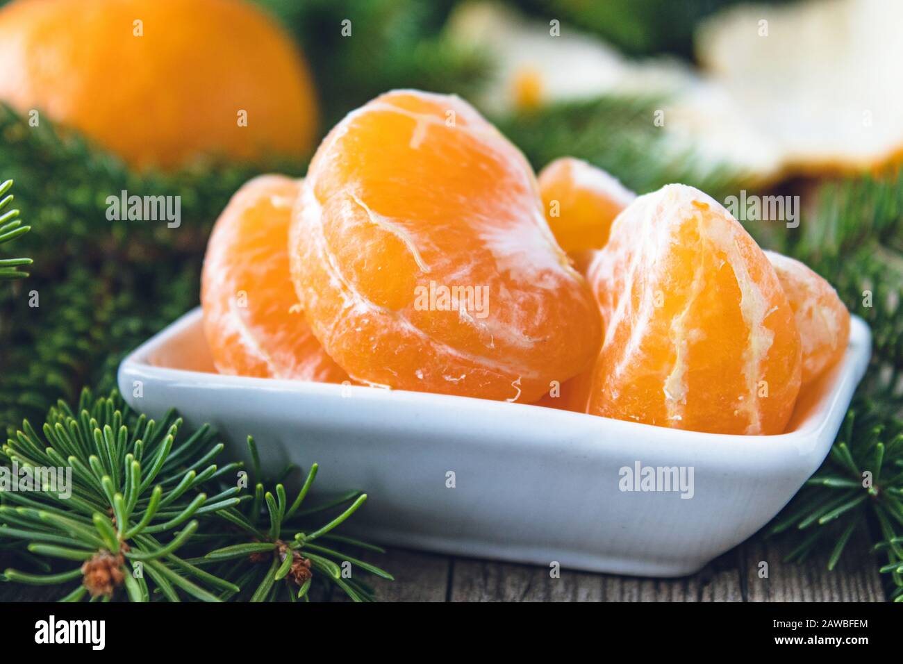 Scheiben reifer gelber Mandarinen liegen in einer Schüssel neben den grünen Zweigen eines Weihnachtsbaums. Zitrusfrüchte, Mandarinen oder Orangen. Nahaufnahme. Stockfoto
