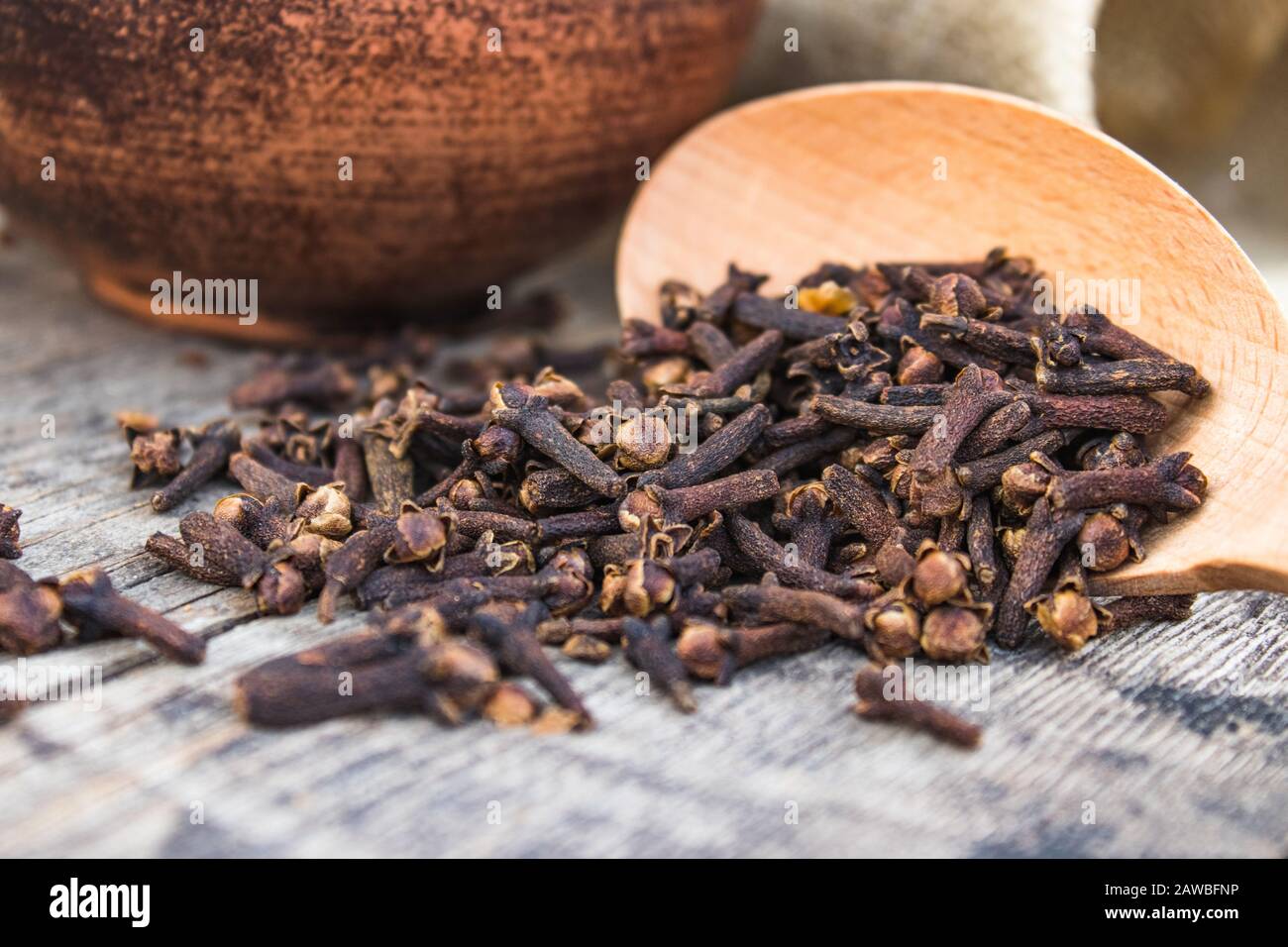 Ein Gewürz getrockneter Nelken liegt auf einem Holzlöffel und ist auf alten Holztafeln verstreut. Gewürznelken zum Kochen. Nahaufnahme. Stockfoto