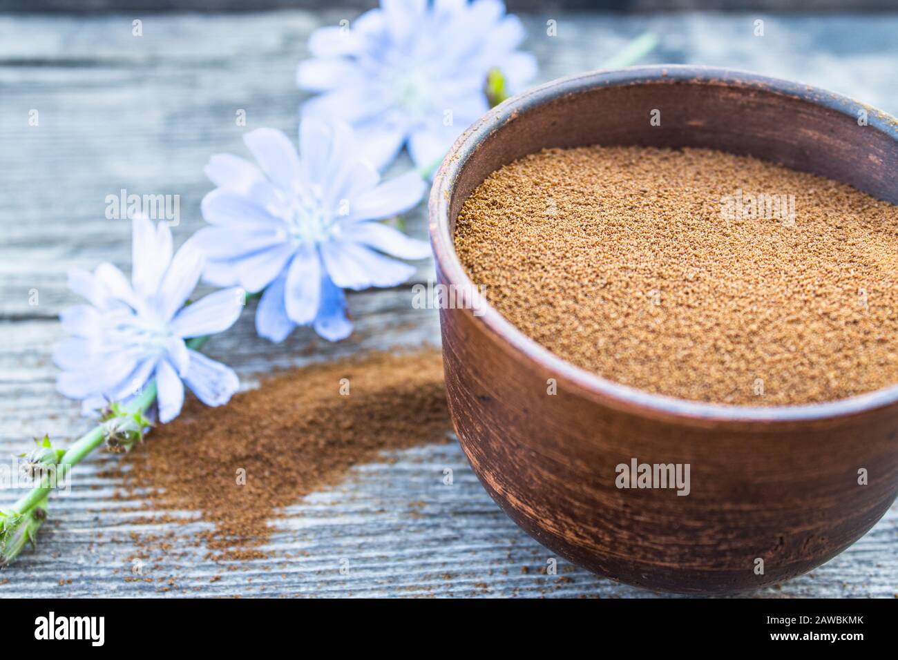 Blaue Zichorienblume und eine Schüssel mit Instant-Zichorienpulver auf einem alten Holztisch. Zichorienpulver. Das Konzept des gesunden Essens eines Getränks. Kaffee substit Stockfoto