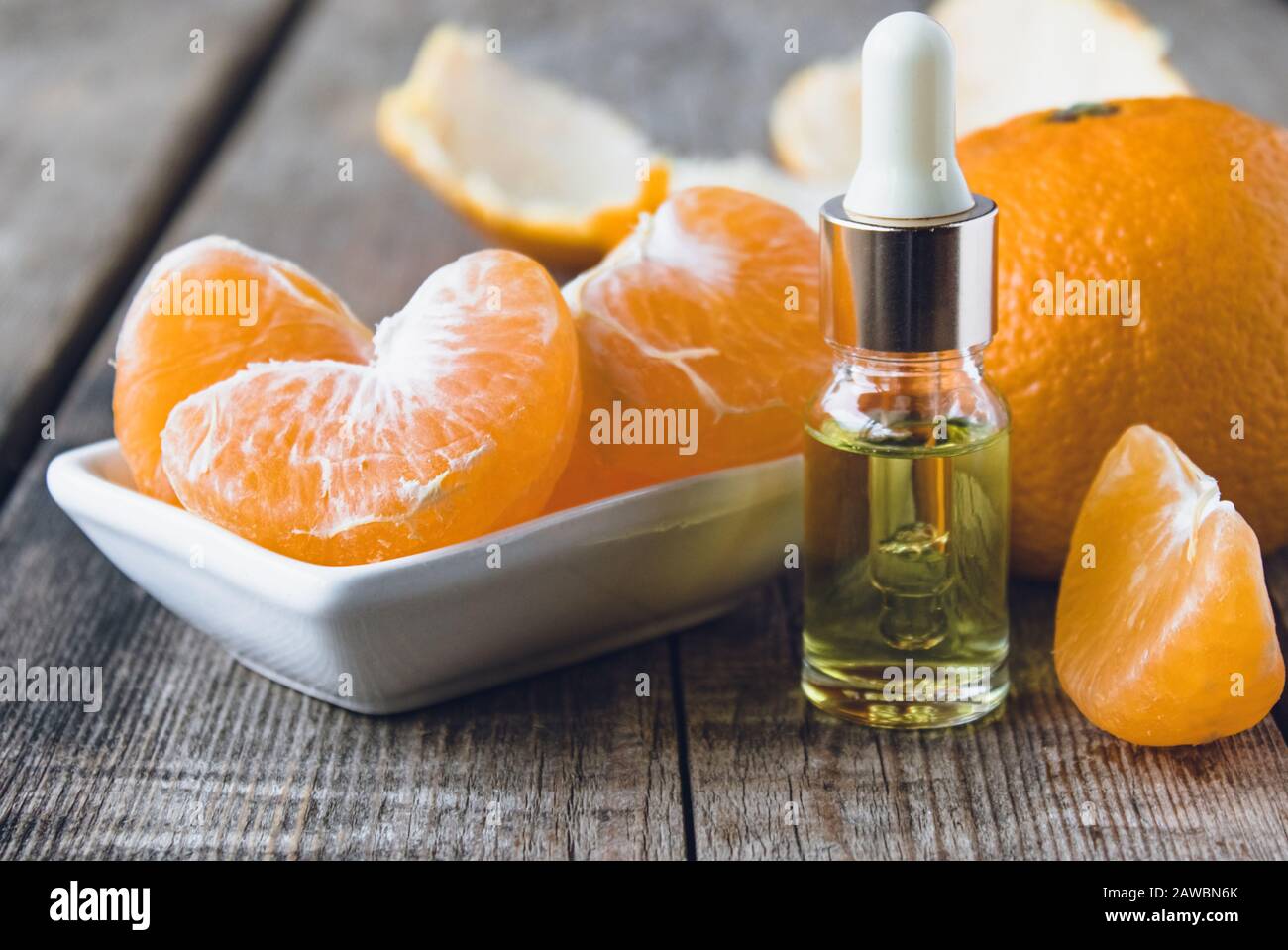 Mandarin ätherisches Öl in einer Glasflasche in der Nähe einer weißen Schüssel mit Scheiben Mandarin. Zitrusfrüchte, Mandarinen oder Orangen. Alternative Medizin Stockfoto