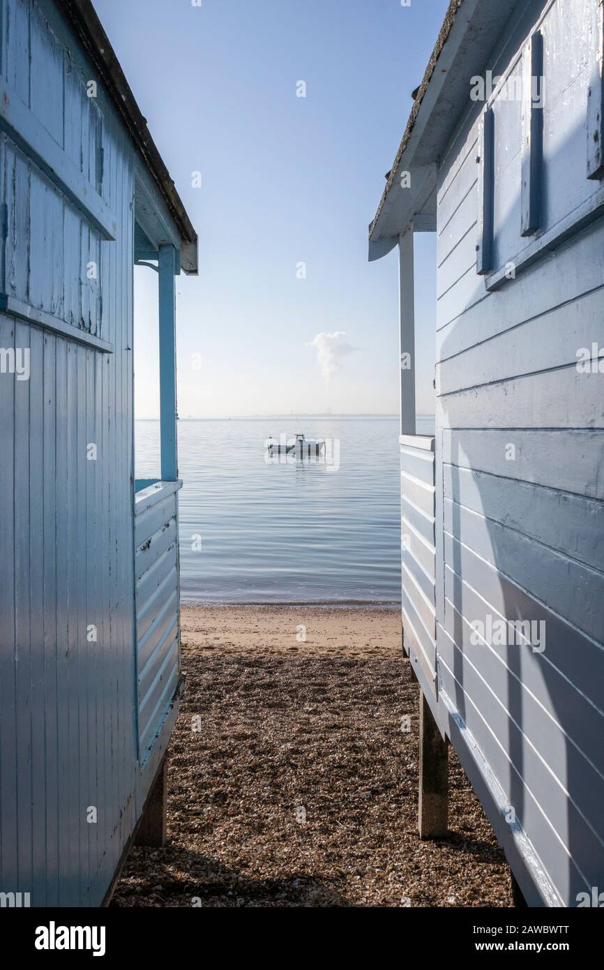 Blaues Boot an einem ruhigen Tag durch die Strandhütten am Strand von Thorpe Bay, Essex, England Stockfoto