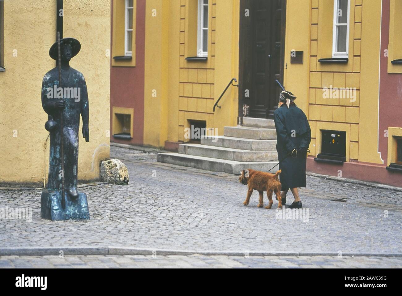 Eine Frau, die ihren Hund von der Bronzestatue eines St. Jakobus Pilgrim Oettinger, Ottingen, Kreis Donau-Ries, in Schwaben, Bayern, Deutschland, spaziert Stockfoto