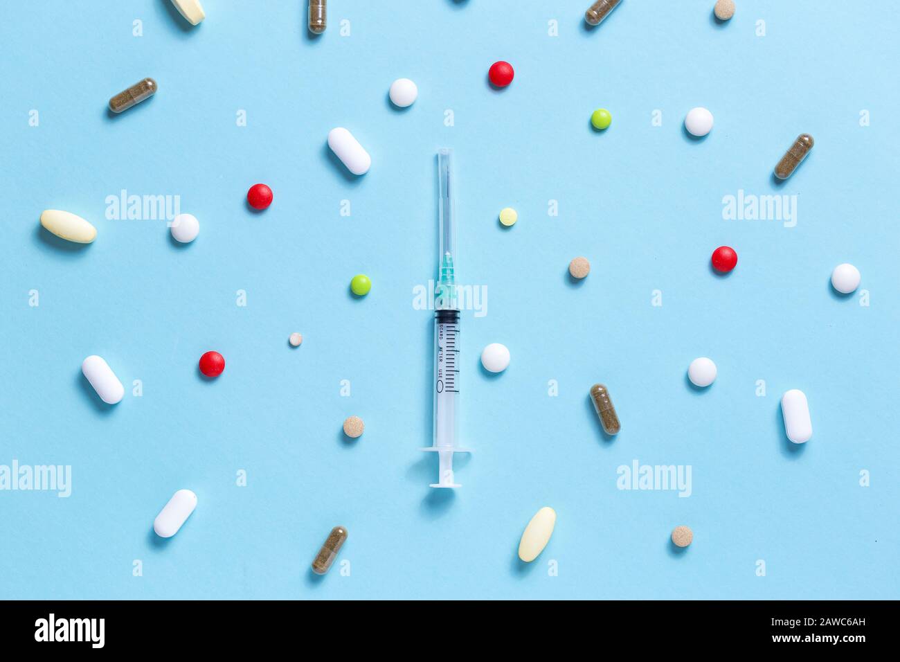 Medizinische Spritze mit vielen farbigen Pillen über blauem Hintergrund. Impfkonzept, Prävention. Stockfoto