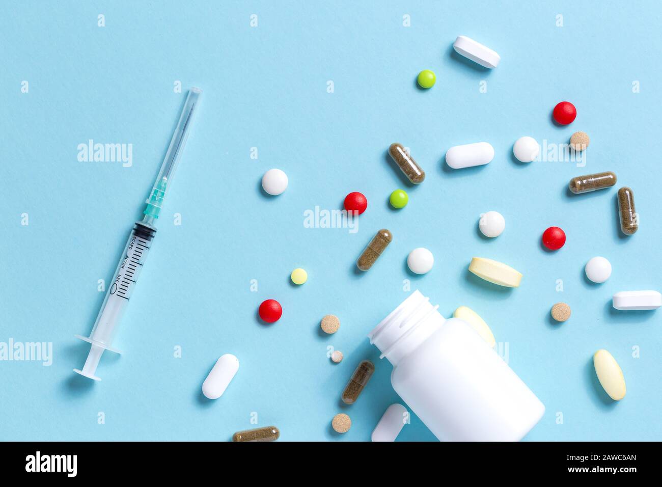 Spritze in der Nähe eines Röhrchens mit Medikamenten und vielen farbigen Pillen über blauem Hintergrund mit Platz für Text Stockfoto