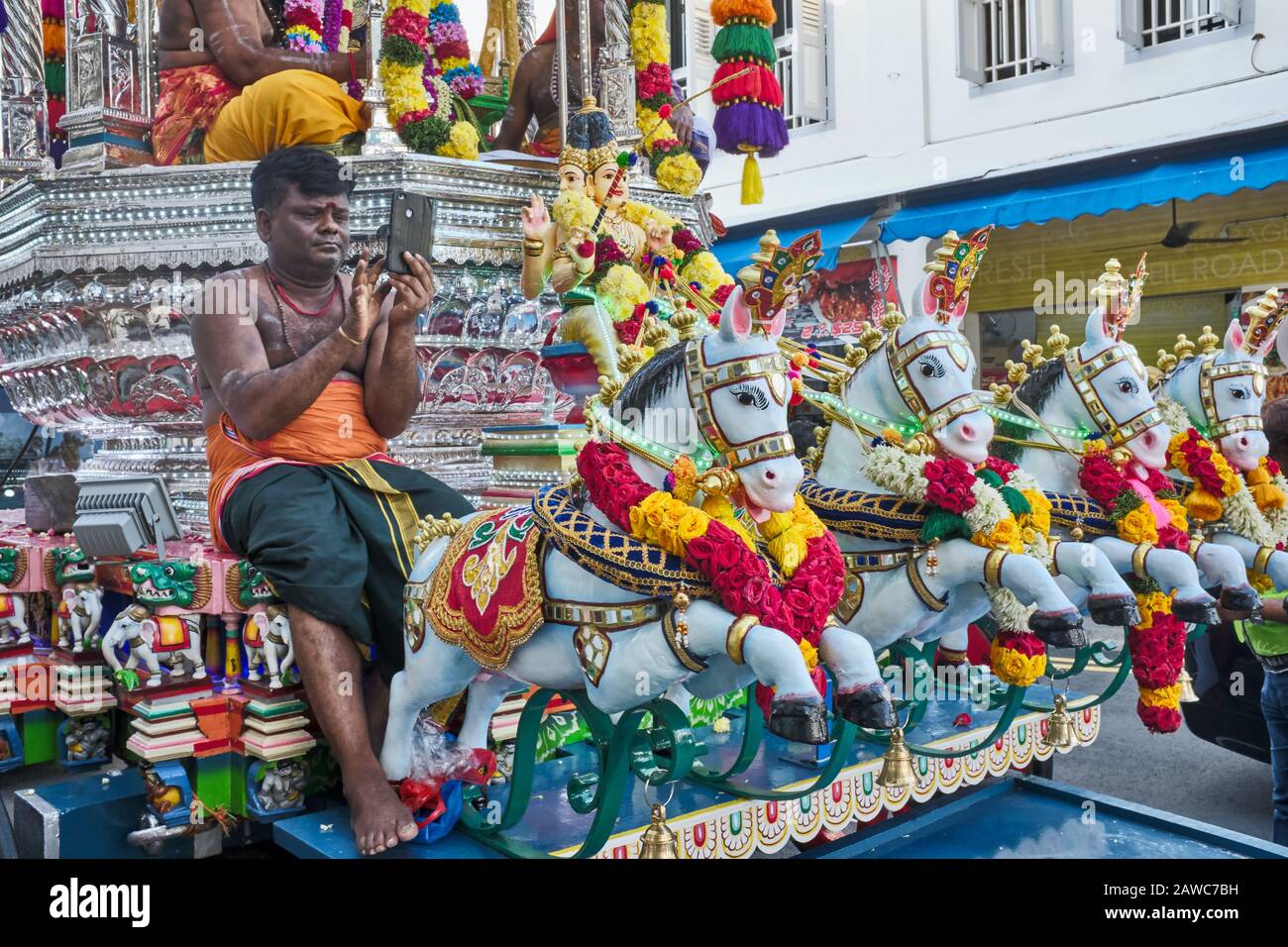 Während des Hindu-Festivals in Thaipusam sitzt ein Teilnehmer auf einem festlichen Wagen mit seinem Handy, Singapur Stockfoto