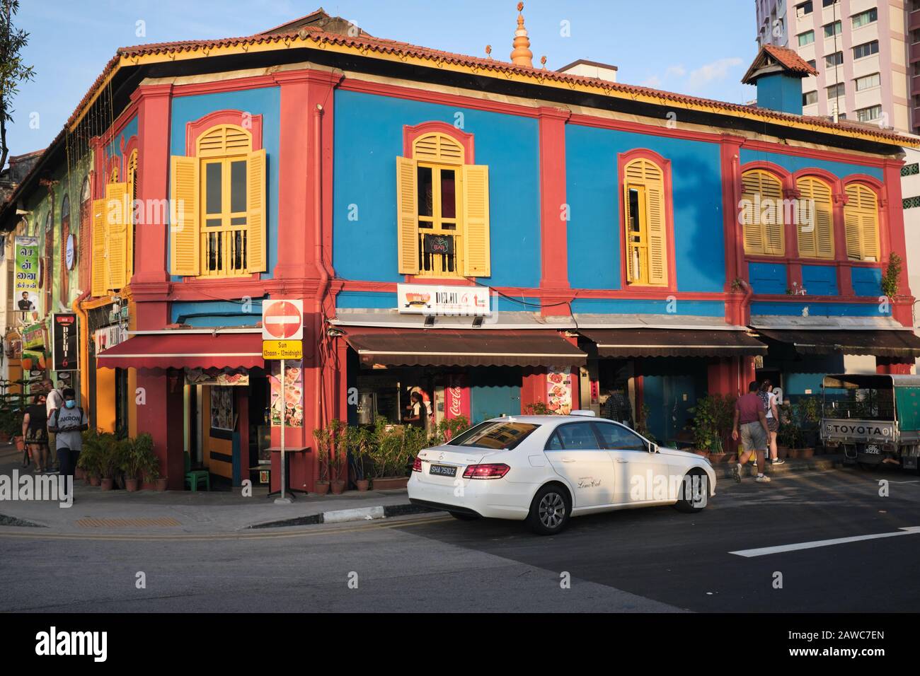 Ein farbenfrohes altes Gebäude mit indischem Restaurant 'Delhi 6', in Little India Area, Singapur, mit einem weißen Mercedes-Taxi davor Stockfoto