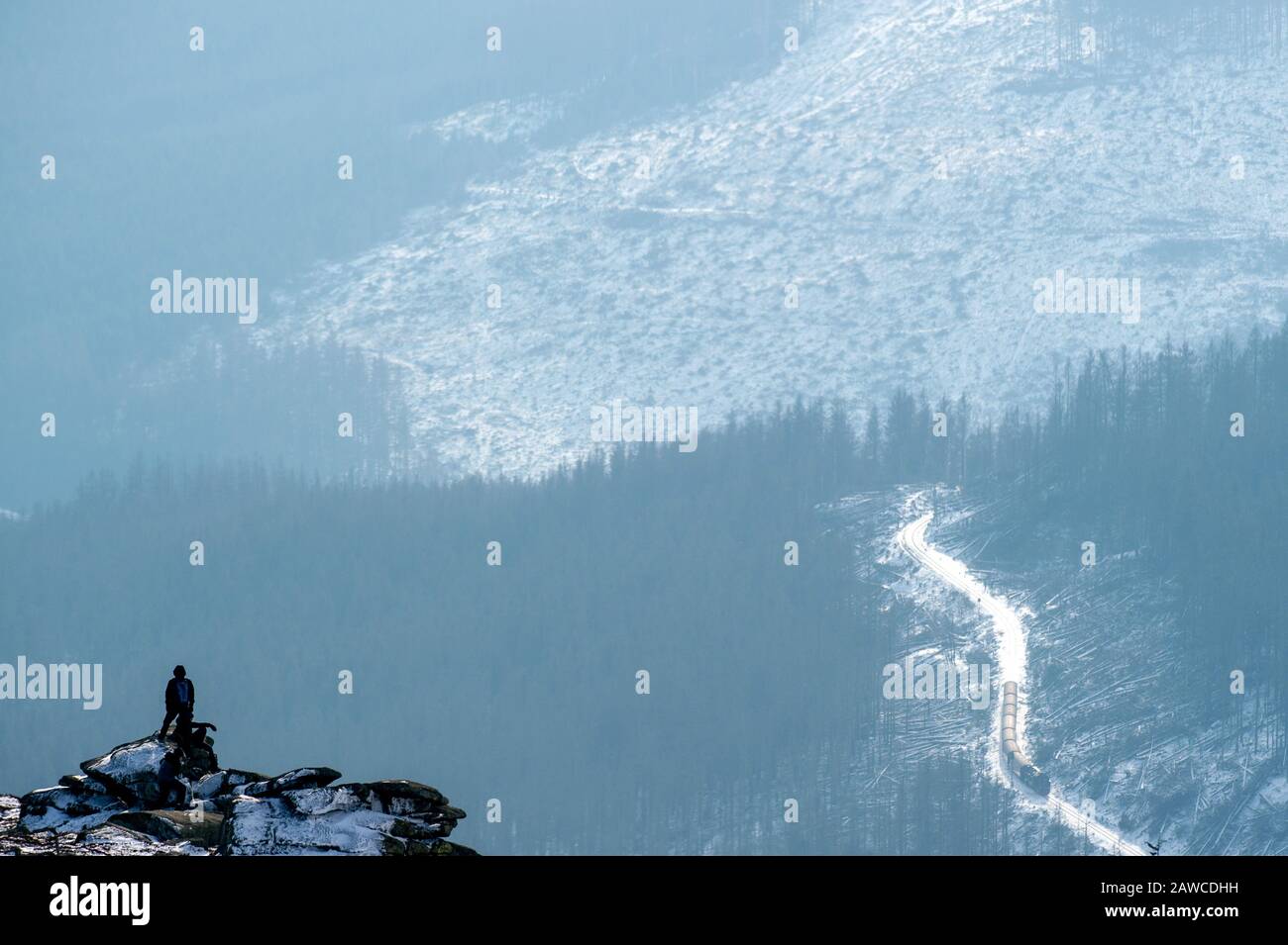 Wernigerode, Deutschland. Februar 2020. Auf einem Felsen auf dem Brockengipfel steht ein Tourist, im Hintergrund fährt ein Zug der Harzer Schmalspurbahnen (HSB) auf die höchste Erhebung des Harzes zu. Das Wetter im Harz dürfte sich in den kommenden Tagen grundlegend ändern. In der Nacht zum Montag erreicht ein Sturmtief die Region. Dann kann der Wind auch im Tiefland Hurrikankraft erreichen. Kredit: Klaus-Dietmar Gabbert / dpa-Zentralbild / dpa / Alamy Live News Stockfoto