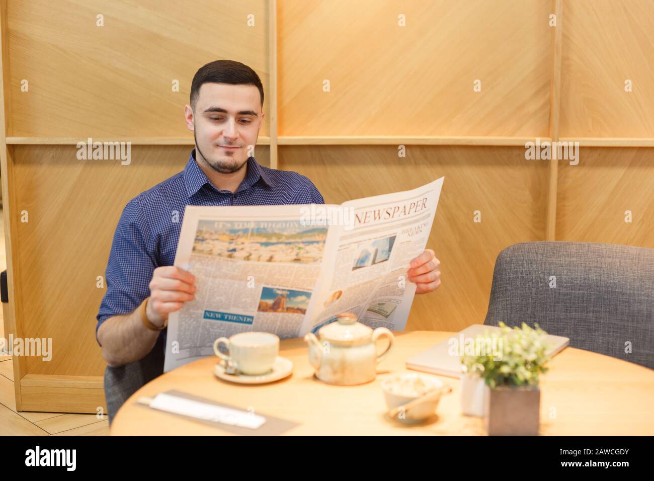 Junger Mann, der morgens die Zeitung liest. Sitzendes Café Stockfoto