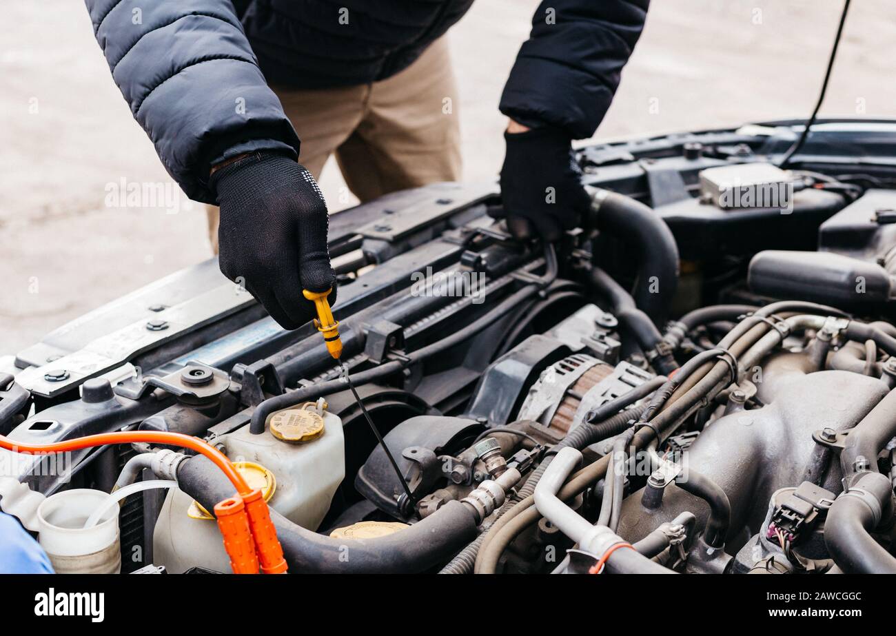 Mann mit schwarzen Handschuhen, der den Ölstand im Auto im Winter im Freien überprüft. Kfz-Mechaniker, der im Kfz-Reparaturdienst arbeitet. Stifthände zur Befestigung eines Autos Stockfoto