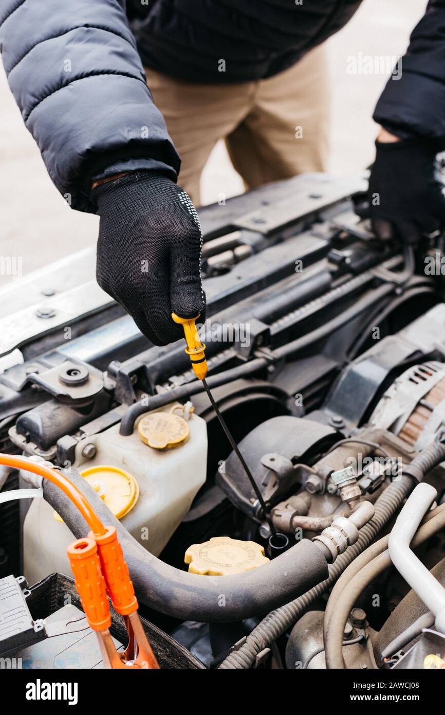 Mann mit schwarzen Handschuhen, der den Ölstand im Auto im Winter im Freien überprüft. Kfz-Mechaniker, der im Kfz-Reparaturdienst arbeitet. Stifthände zur Befestigung eines Autos Stockfoto