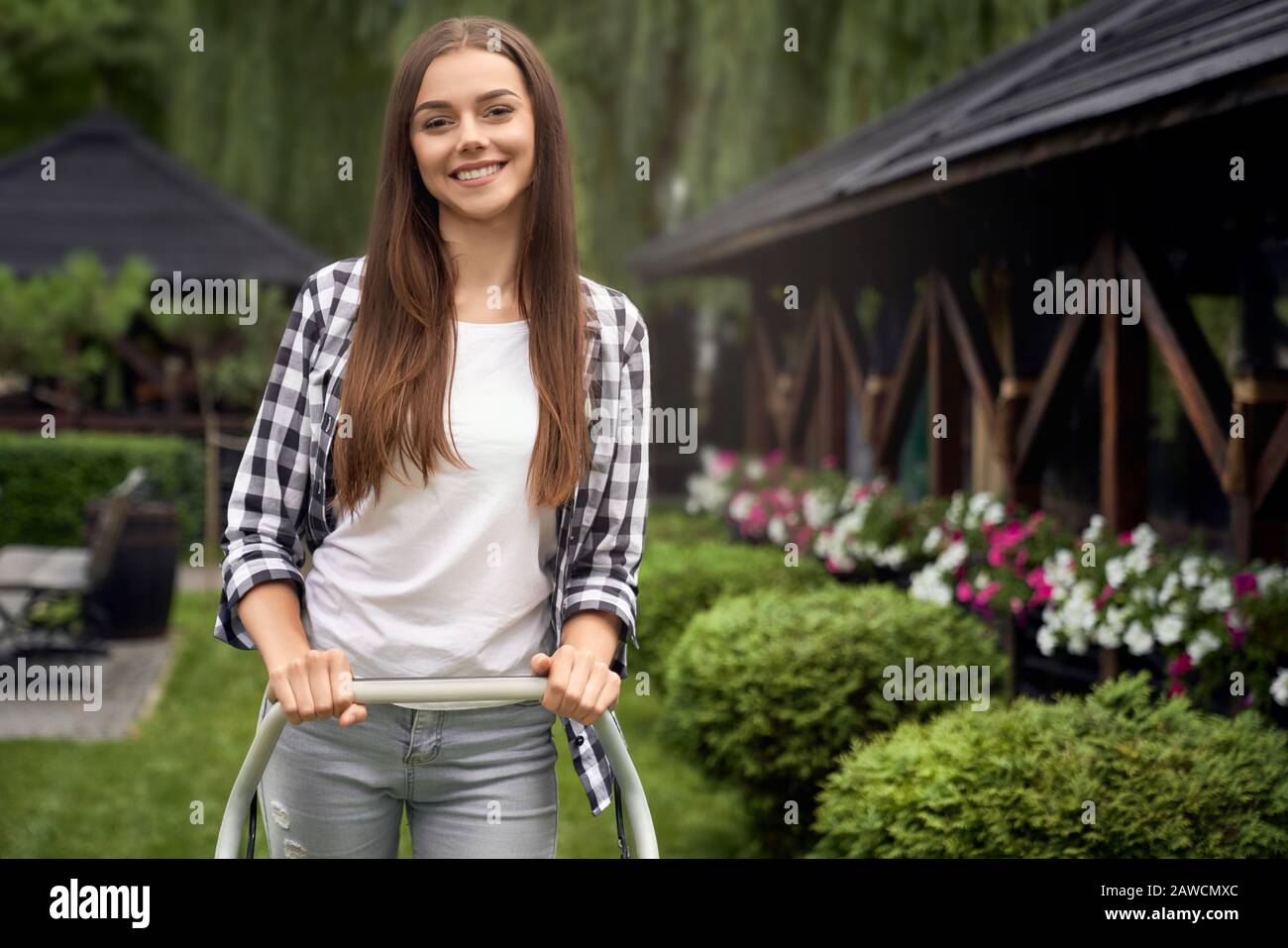 Vorderansicht einer hübschen jungen lächelnden Frau mit Maschine auf dem Hinterhof, mit Blick auf die Kamera. Portrait von Gärtnerinnen, die im Sommer mit Haltegriff arbeiten. C Stockfoto