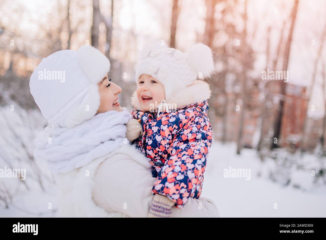 Winterspaziergang verschneiten Wald im Morgengrauen. Fröhliche junge Mutter hält kleine fröhliche Tochter in den Armen, sie lachen Stockfoto