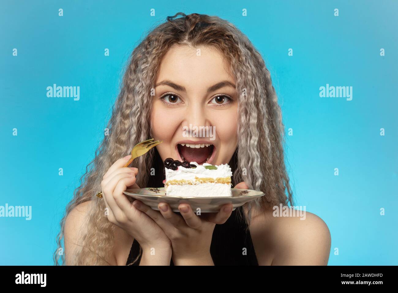 Fröhliche junge Frau mit cremefarbenem Dessert, überbissend, gruselig, auf zyanischem Hintergrund schreiend Stockfoto