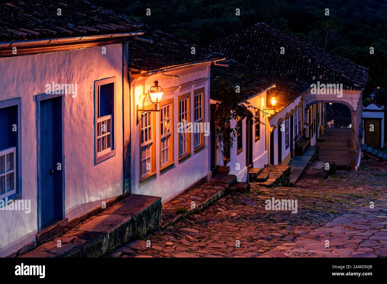 Blick auf eine alte gepflasterte Straße und die Häuser im Kolonialstil, die von Laternen in der historischen Stadt Tiradentes in Minas Gerais angezündet werden Stockfoto
