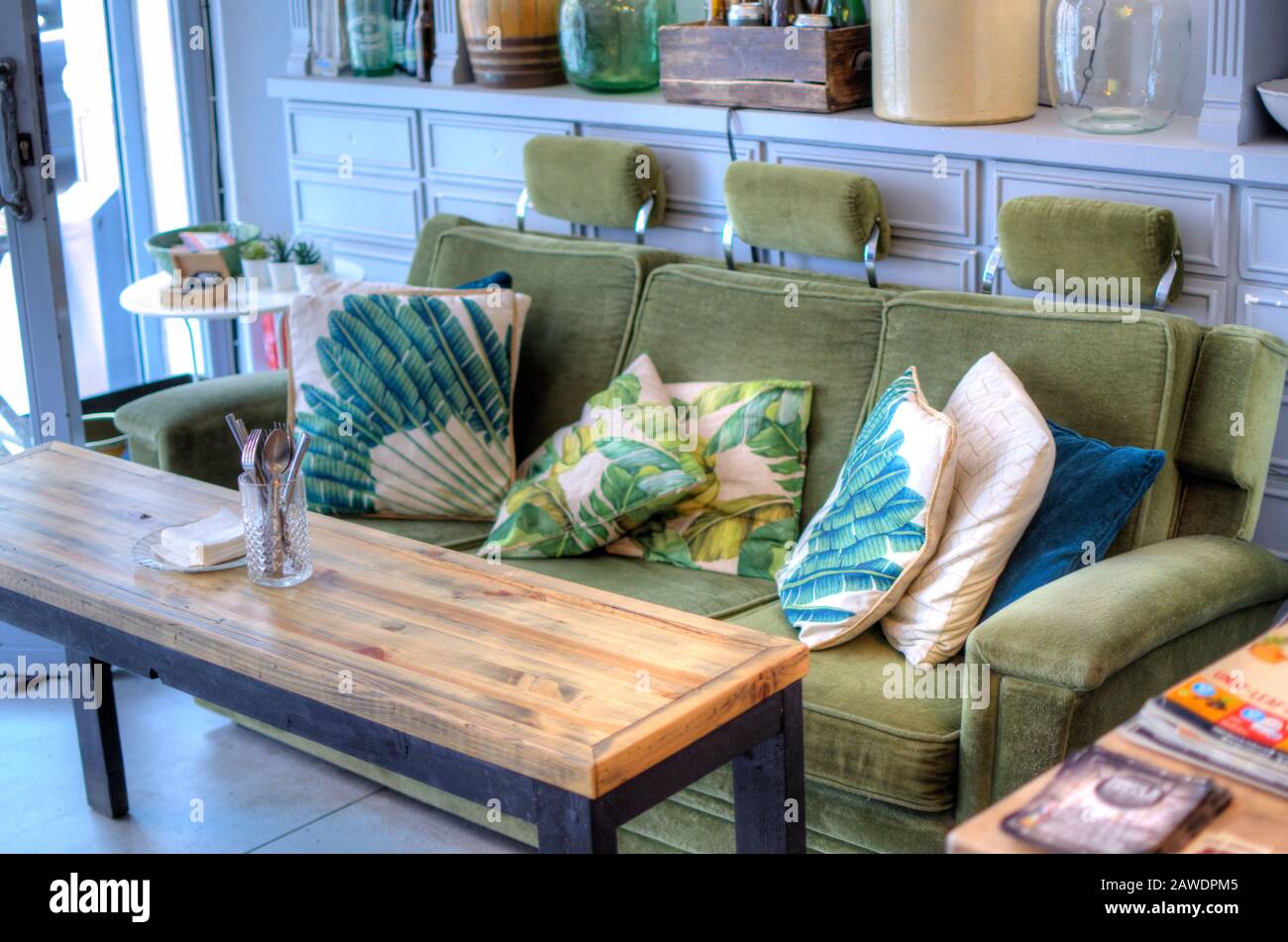 Innenbereich einer Bar. Grüne Couch mit bunten Kissen. Selektives Fokussieren auf das Besteck am Holztisch. Hopfen & D. Stockfoto