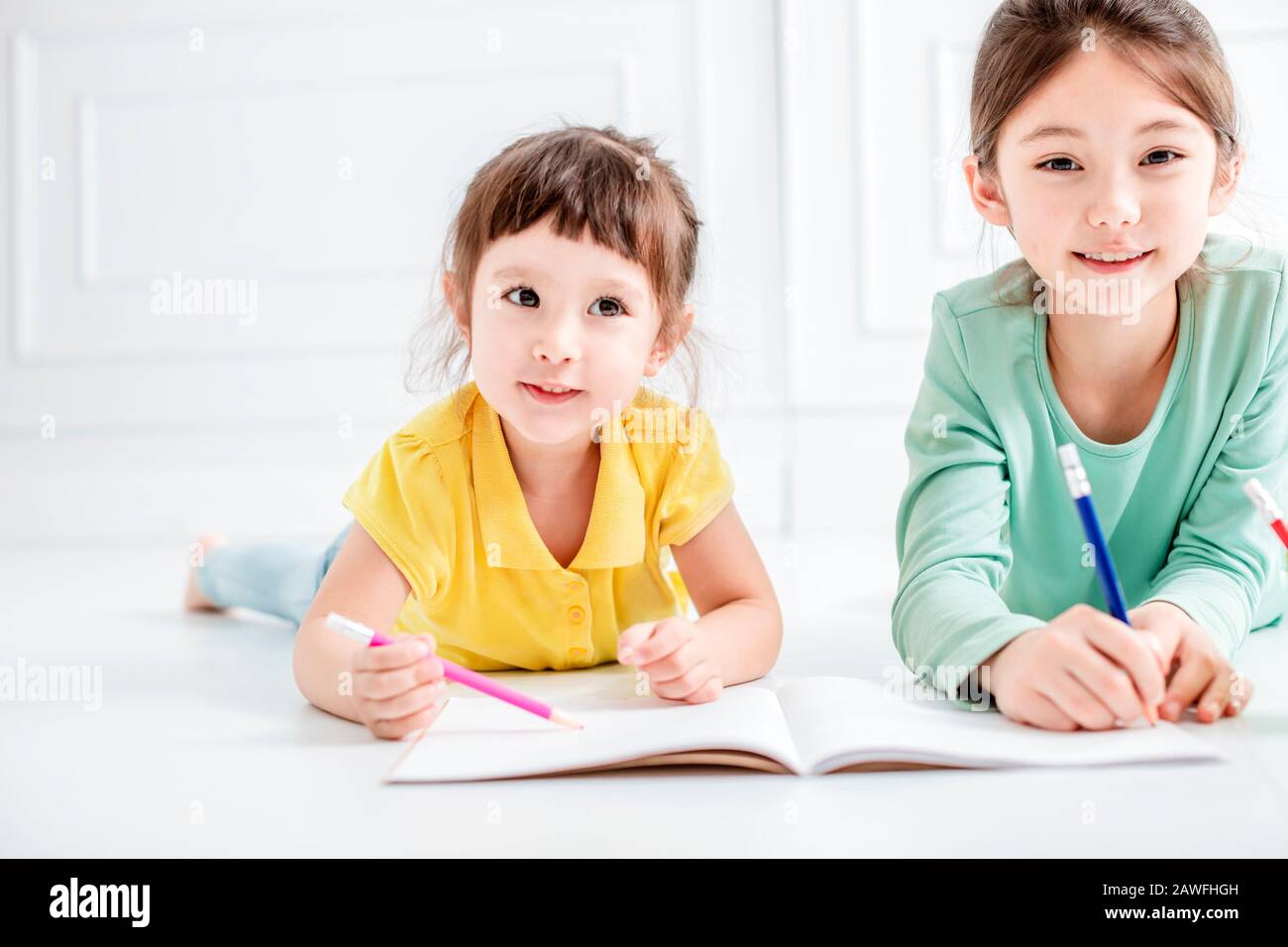 Glückliche zwei kleine Mädchen zeichnen und machen Hausaufgaben auf dem Flor Stockfoto