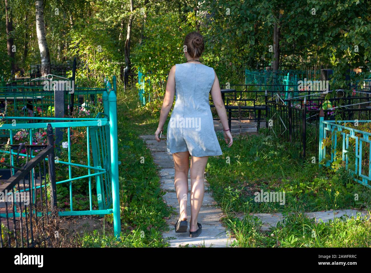 Ein Mädchen läuft durch den Friedhof. Russischer Friedhof im Wald. Das Mädchen im Kleid wanderte in einen unbekannten Teil des Stadtparks. Gefährlich Stockfoto