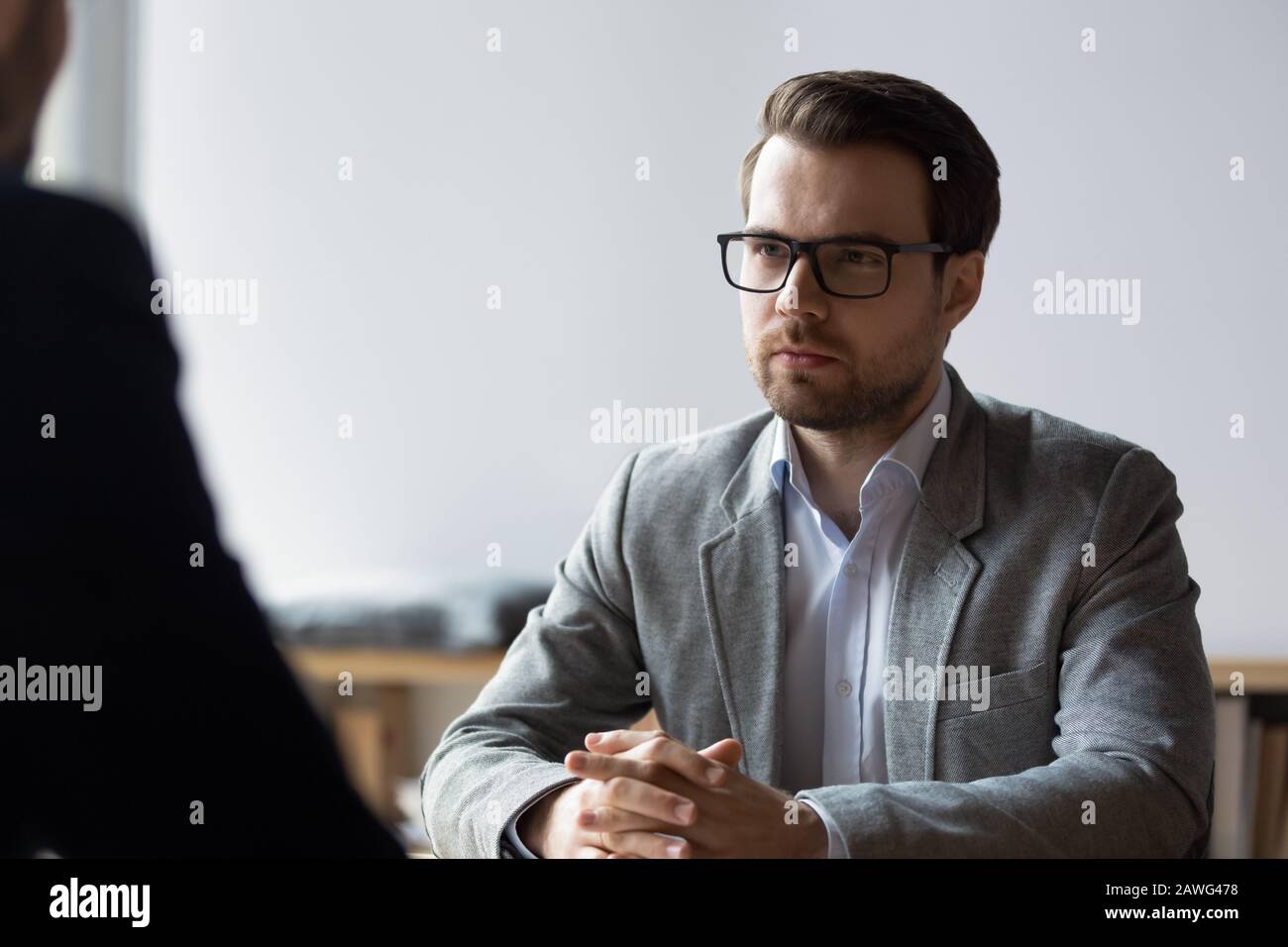 Ernsthafter Geschäftsmann mit verschlaffenen Händen, der Gegner bei Verhandlungen betrachtet Stockfoto